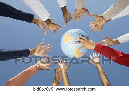 Stock Photo - Multi-ethnic hands reaching for globe ball. Fotosearch