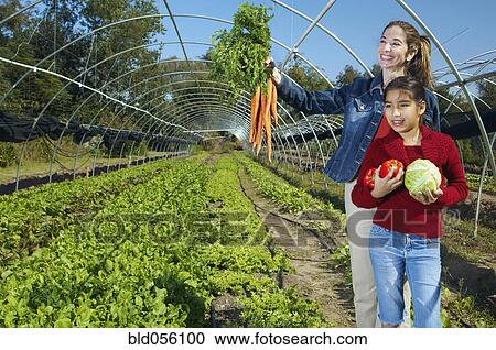 Stock Image - Multi-ethnic mother and daughter harvesting organic produce. Fotosearch
