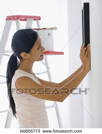 Stock Image - Pacific Islander woman hanging picture. Fotosearch