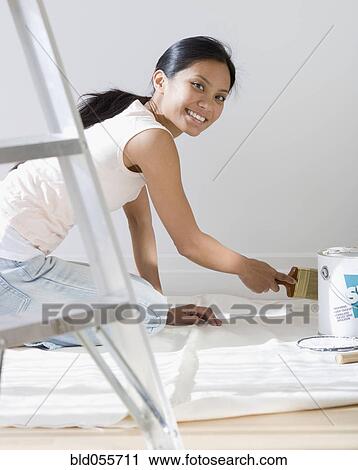 Stock Image - Pacific Islander woman painting baseboard. Fotosearch