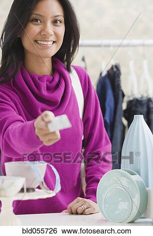 Stock Photograph - Pacific Islander woman paying at boutique with credit card. Fotosearch