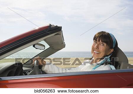 Stock Image - Senior Hispanic woman driving convertible car. Fotosearch