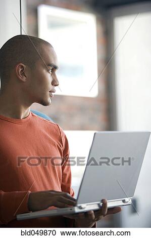 Stock Image - African American man holding laptop. Fotosearch