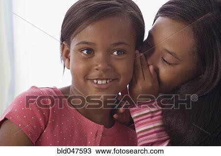 Stock Image - African American sisters telling secret. Fotosearch
