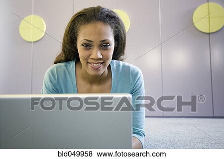Stock Photo - African American woman using laptop on floor. Fotosearch