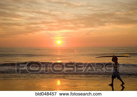 Stock Photo - Asian boy carrying surfboard at beach. Fotosearch