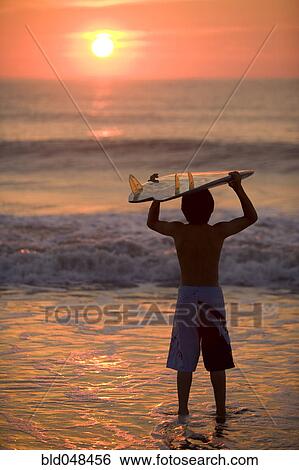 Asian boy holding surfboard at beach View Large Photo Image Stock Photograph - Asian boy holding surfboard at beach. Fotosearch