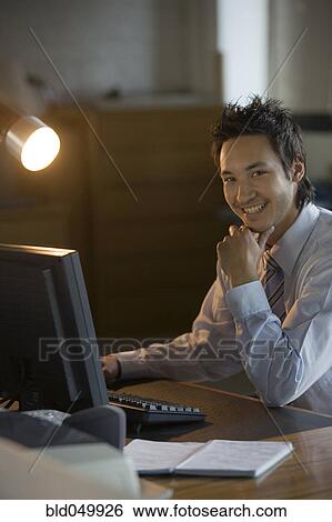 Stock Photograph - Asian businessman sitting at computer. Fotosearch