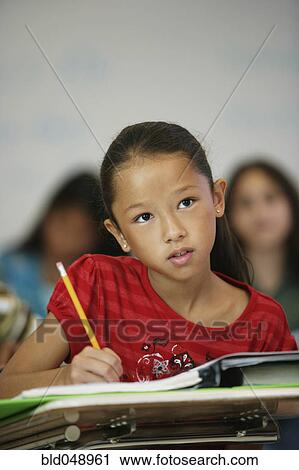 Stock Image - Asian girl at desk in classroom. Fotosearch