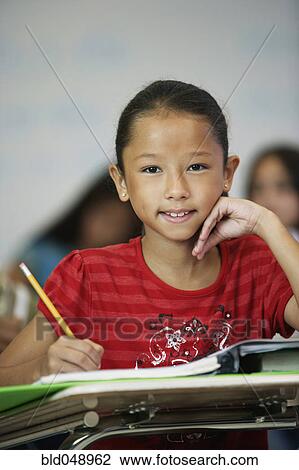 Stock Image - Asian girl at desk in classroom. Fotosearch