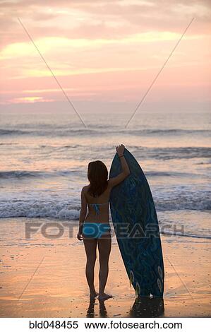 Stock Photography - Asian girl holding surfboard at beach. Fotosearch