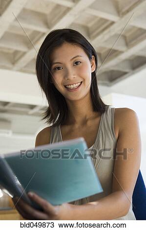Stock Image - Asian woman holding open notebook. Fotosearch