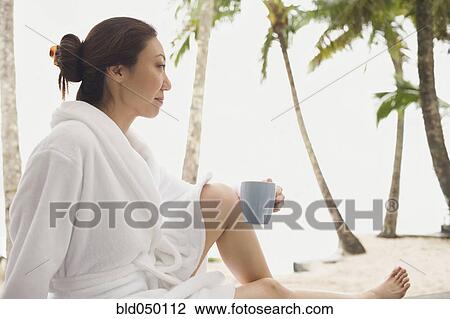 Stock Image - Asian woman in bathrobe holding mug. Fotosearch