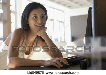 Stock Photography - Asian woman sitting at computer. Fotosearch