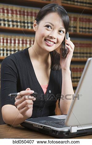 Stock Photo - Asian woman talking on cell phone in library. Fotosearch