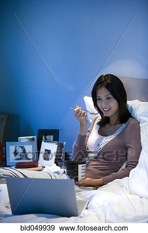Stock Photo - Asian woman watching laptop in bed. Fotosearch