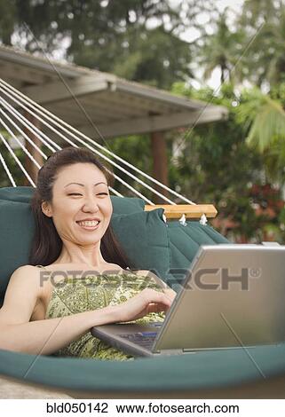 Stock Image - Asian woman with laptop in hammock. Fotosearch