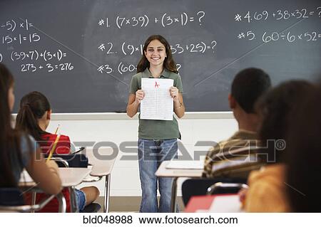 Girl holding up paper in front of class View Large Photo Image Stock Photo - Girl holding up paper in front of class. Fotosearch