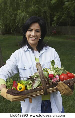 Stock Image - Hispanic woman holding fresh vegetables. Fotosearch