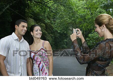 Stock Image - Hispanic woman taking photograph of couple. Fotosearch