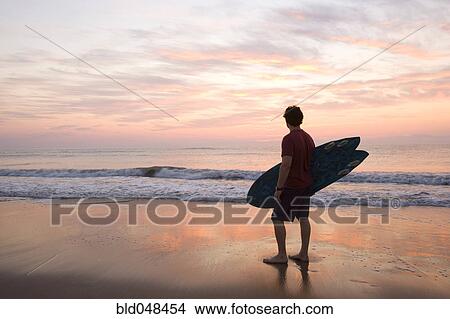 Man holding surfboard at beach View Large Photo Image Picture - Man holding surfboard at beach. Fotosearch