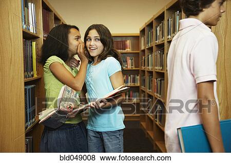 Stock Photo - Multi-ethnic girls telling secret in library. Fotosearch