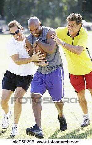 Stock Photograph - Multi-ethnic men playing football. Fotosearch