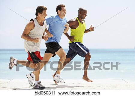 Stock Image - Multi-ethnic men running in beach. Fotosearch
