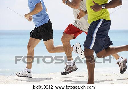 Stock Image - Multi-ethnic men running in beach. Fotosearch