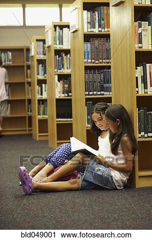 Stock Image - Multi-ethnic students reading library book. Fotosearch