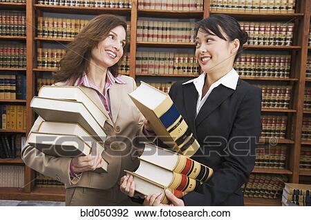 Stock Image - Multi-ethnic women carrying stacks of library reference books. Fotosearch