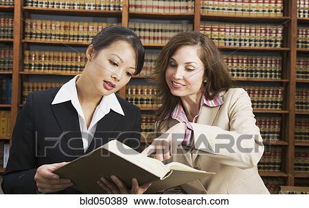 Multi-ethnic women looking at library reference book View Large Photo Image Stock Photo - Multi-ethnic women looking at library reference book. Fotosearch