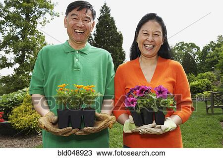 Stock Image - Senior Asian couple holding potted plants. Fotosearch