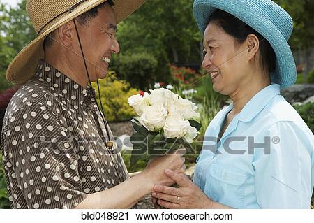 Stock Image - Senior Asian man giving flowers to wife. Fotosearch