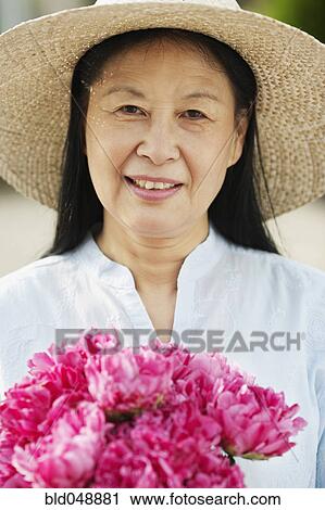 Stock Image - Senior Asian woman holding flowers. Fotosearch