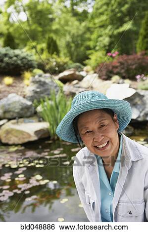 Stock Photograph - Senior Asian woman next to pond. Fotosearch
