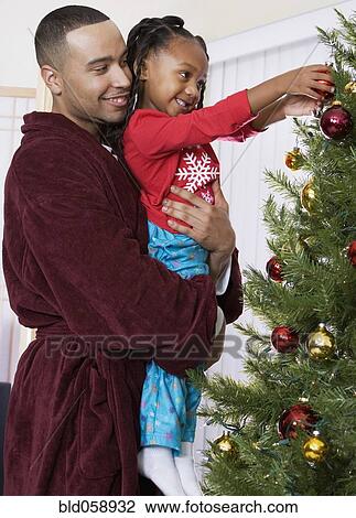 Stock Image - African father and daughter decorating Christmas tree. Fotosearch