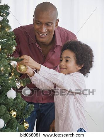 Stock Image - African father and son decorating Christmas tree. Fotosearch