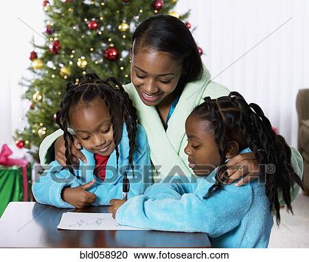 Stock Image - African mother and daughters writing letter to Santa Claus. Fotosearch