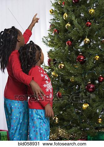 Stock Image - African sisters looking at Christmas tree. Fotosearch