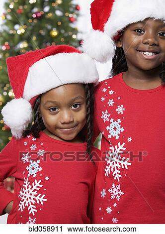 Stock Image - African sisters wearing Santa Claus hats. Fotosearch