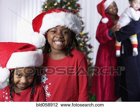 Stock Image - African sisters wearing Santa Claus hats. Fotosearch