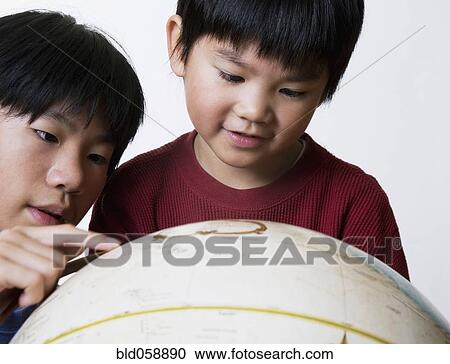 Stock Image - Asian brothers looking at globe. Fotosearch