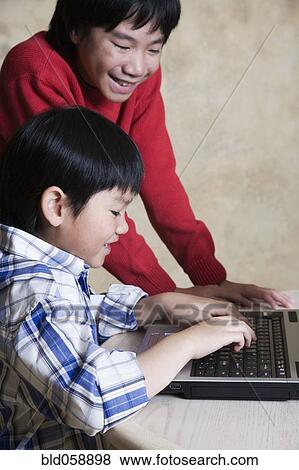Asian brothers looking at laptop View Large Photo Image Stock Photo - Asian brothers looking at laptop. Fotosearch