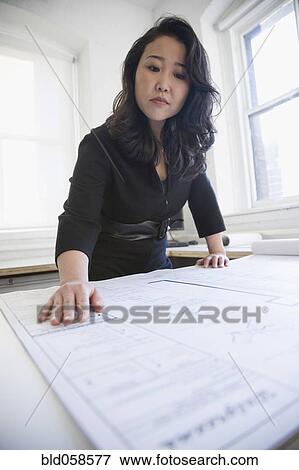 Stock Photo - Asian businesswoman looking at blueprints. Fotosearch