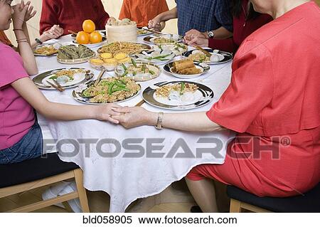 Stock Photography - Asian family praying at dinner table. Fotosearch