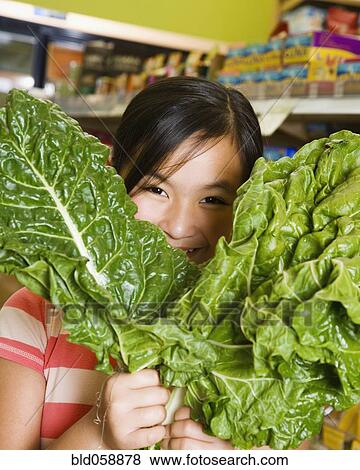 Stock Photo - Asian girl holding green leaf vegetables. Fotosearch