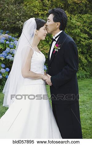 Stock Photography - Asian groom kissing bride’s forehead. Fotosearch