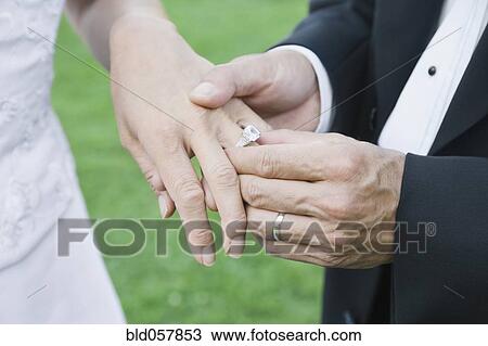 Stock Image - Asian groom putting ring on bride’s finger. Fotosearch