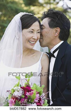 Stock Image - Asian groom telling secret to bride. Fotosearch
